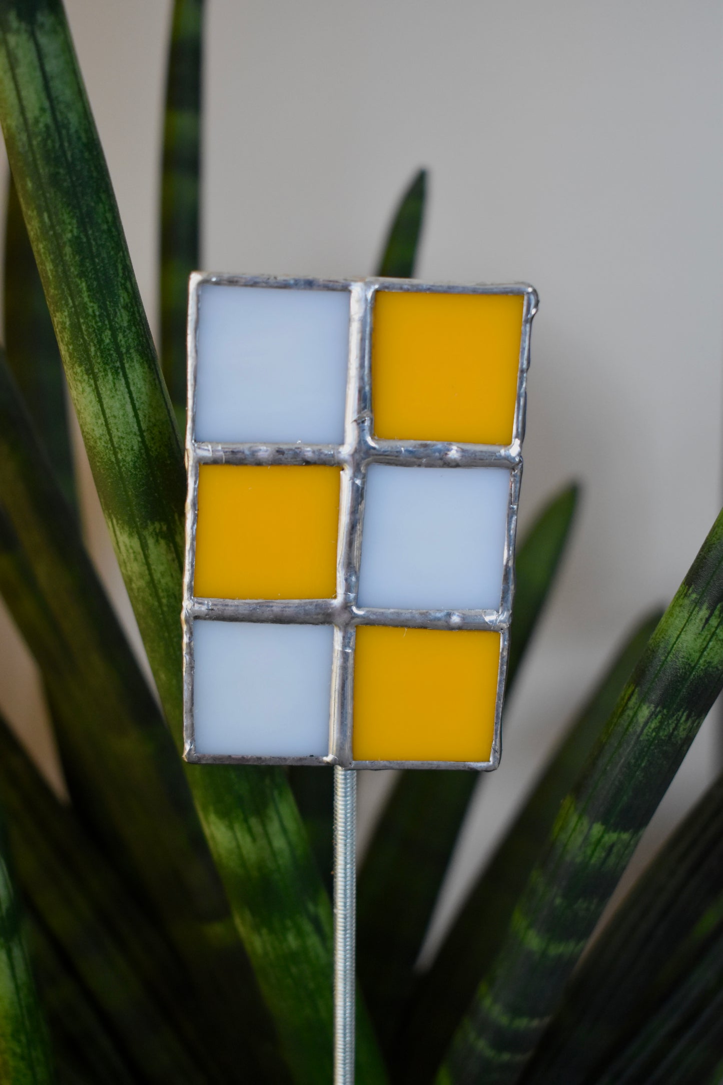 Decorative plant stake with square pattern of orange and white on a blurred green plant background