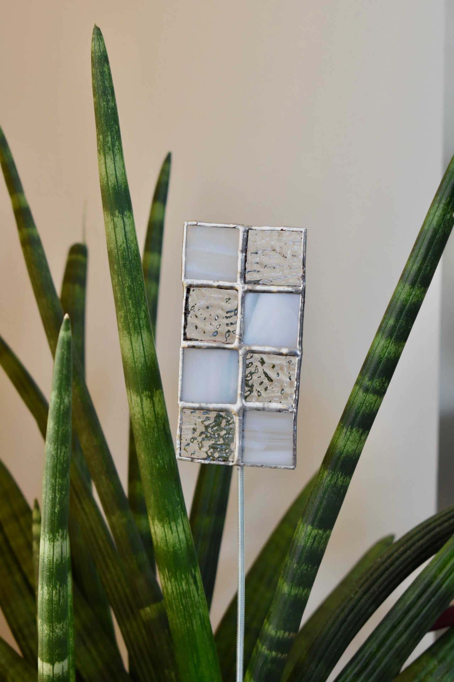 Decorative plant stake with a mosaic design in front of a green plant