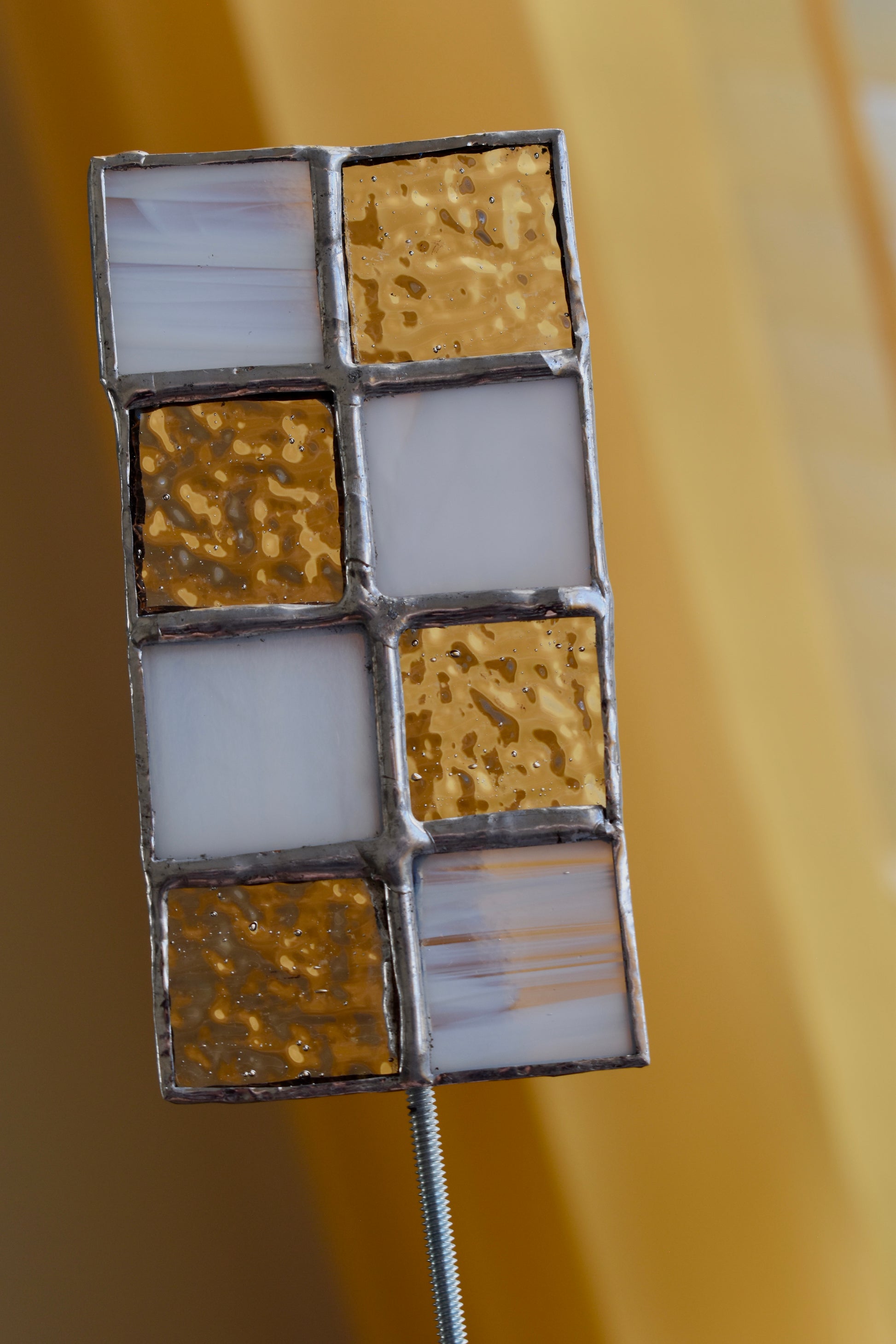 Decorative wall art with square tiles in gold and white on a blurred background