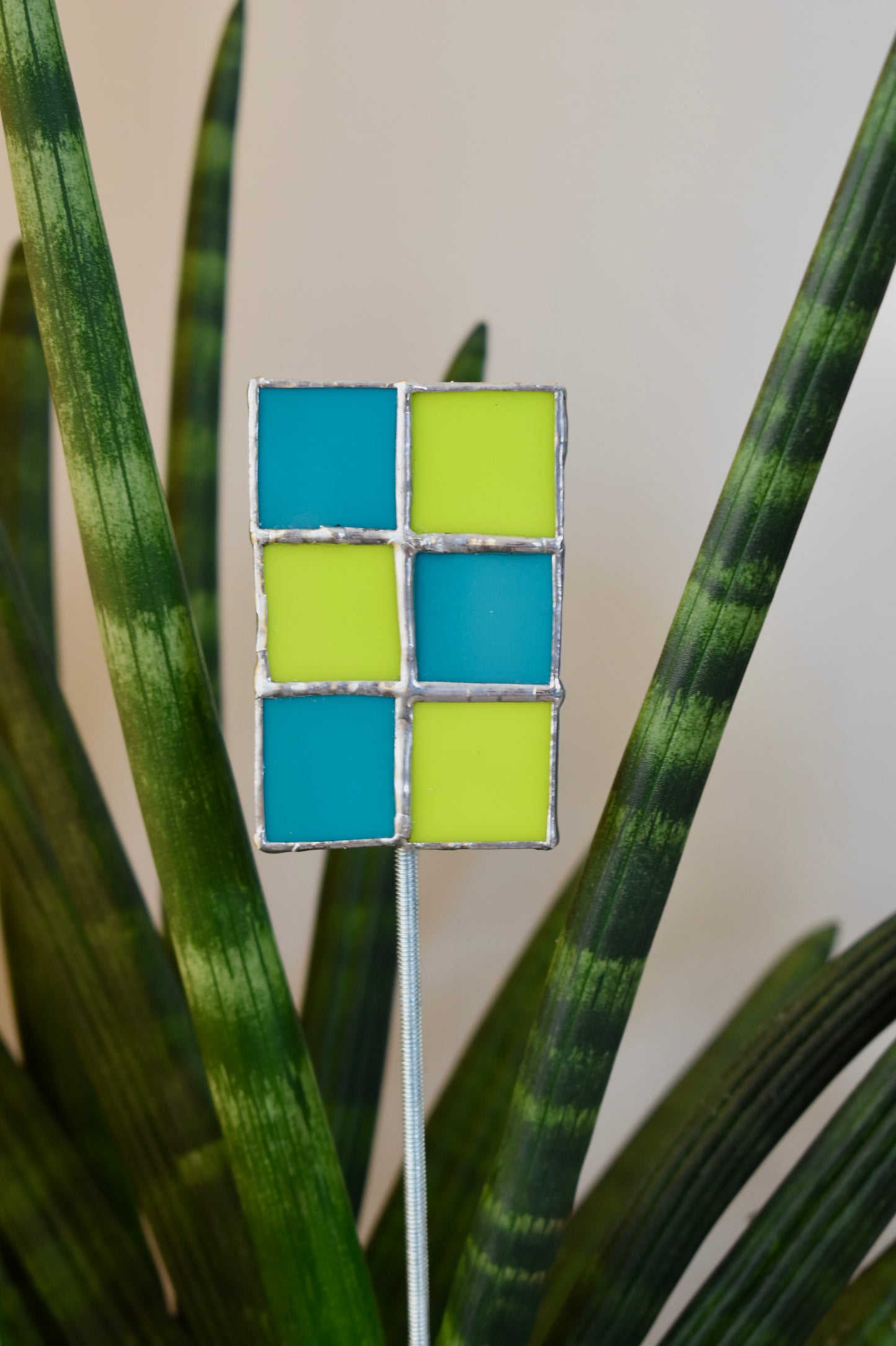 Decorative plant stake with blue and green square pattern among green leaves.