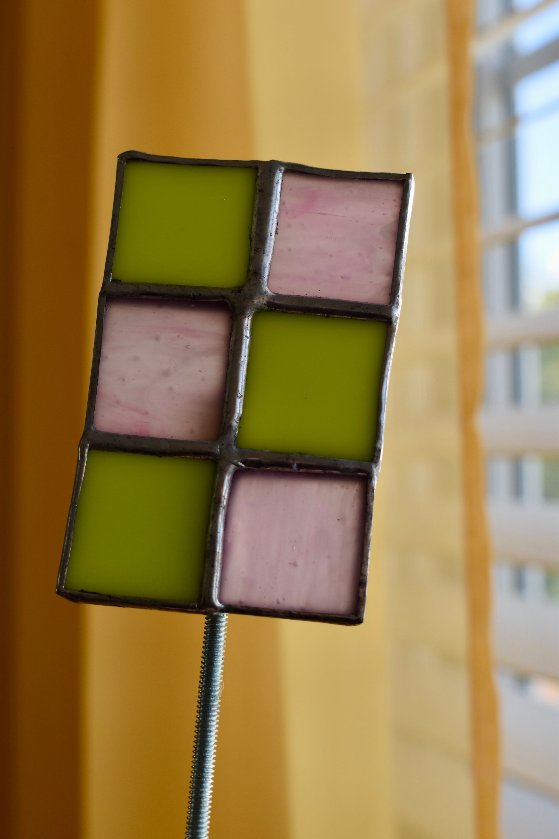 Decorative item with green and pink square tiles on a stand against a blurred background